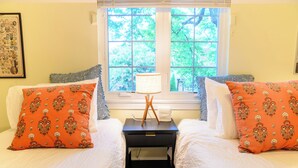 Une chambre avec deux lits, une table de chevet avec une lampe et une fenêtre donnant sur des arbres.