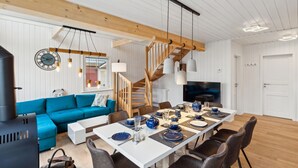A modern living room with a blue sofa, wooden staircase, dining table set for six, and a TV in the background. - Stunning home in Wandlitz OT Zerpenschl with house a panoramic view (Wandlitz OT Zerpenschl)