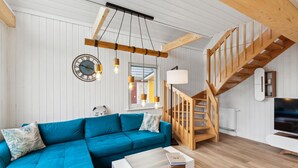 A modern living room with a blue sectional sofa, a wooden staircase, and a large clock on the wall. - Stunning home in Wandlitz OT Zerpenschl with house a panoramic view (Wandlitz OT Zerpenschl)