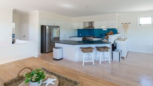 A modern kitchen with white cabinets, a blue backsplash, and a stainless steel refrigerator. There are three bar stools and a small island with a sink. - Sunny Shores Family Retreat: Your Perfect Getaway in West Busselton! (West Busselton)