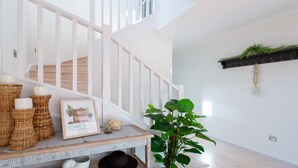 A staircase with white railings, a wicker basket with candles, a framed picture, and a large green plant. - Sunny Shores Family Retreat: Your Perfect Getaway in West Busselton! (West Busselton)