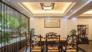 A traditional Japanese-style dining room with a wooden table and chairs, a large window with a view of greenery, and a ceiling light fixture. - Benyuan Hostel (Wuyishan)