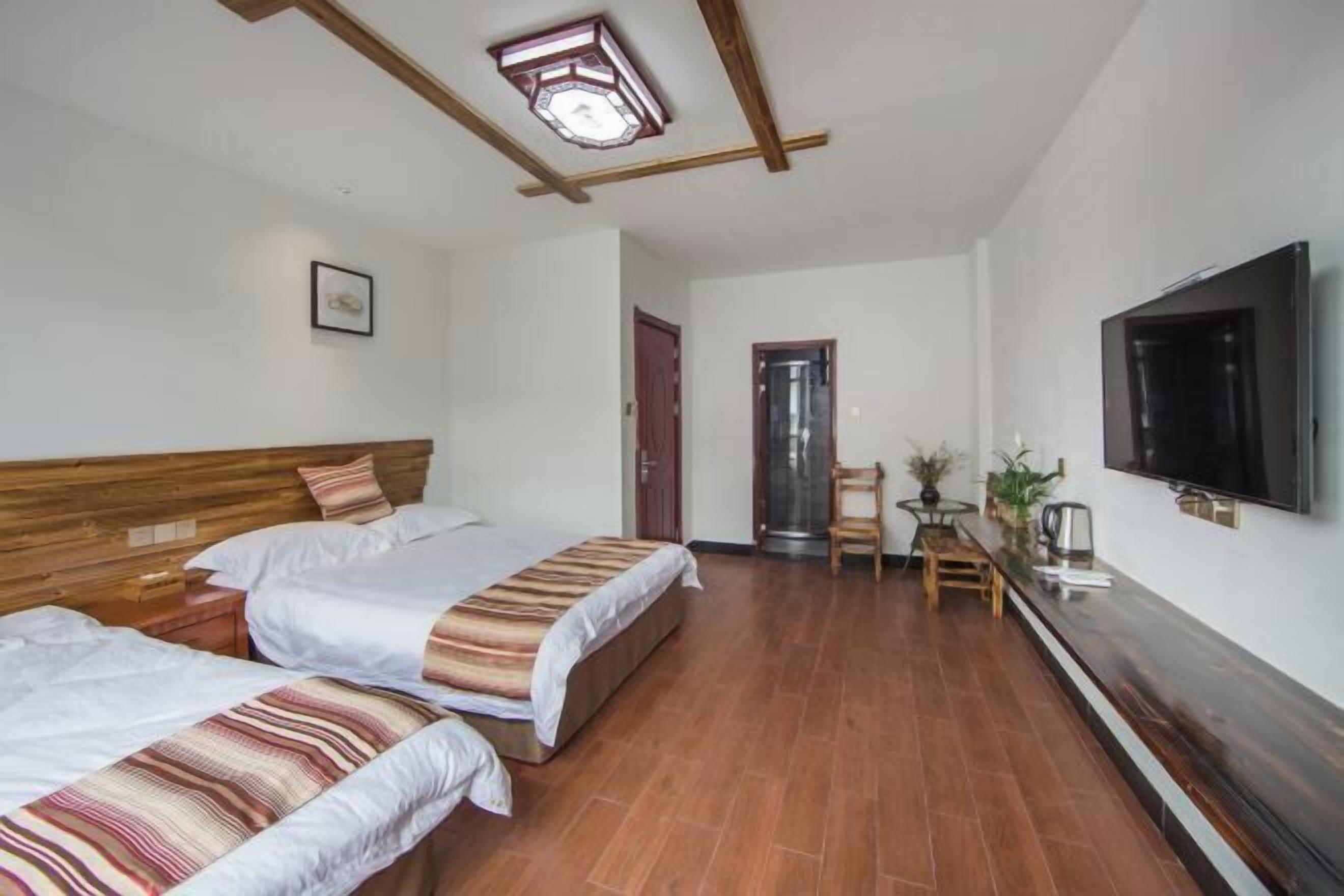 A hotel room with two beds, a TV, a wooden ceiling, and a small table with a chair.