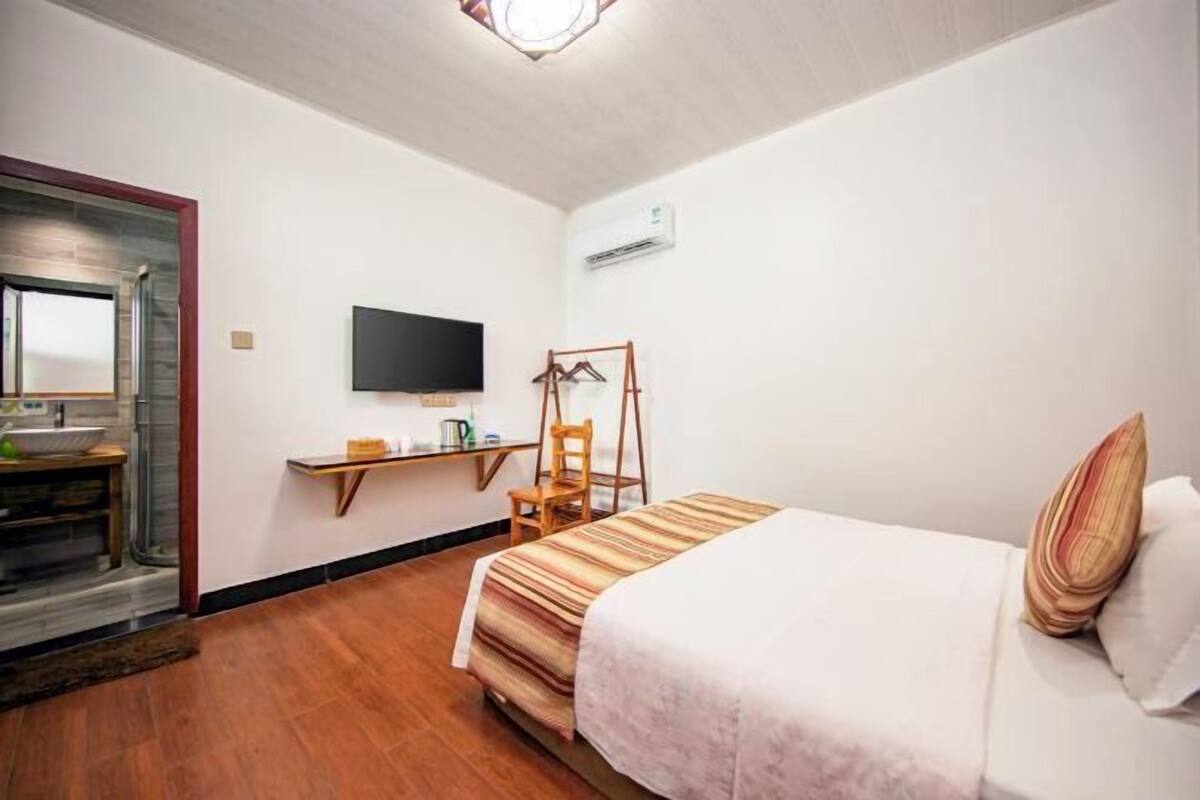 A hotel room with a bed, a desk with a chair, a TV mounted on the wall, and a window.