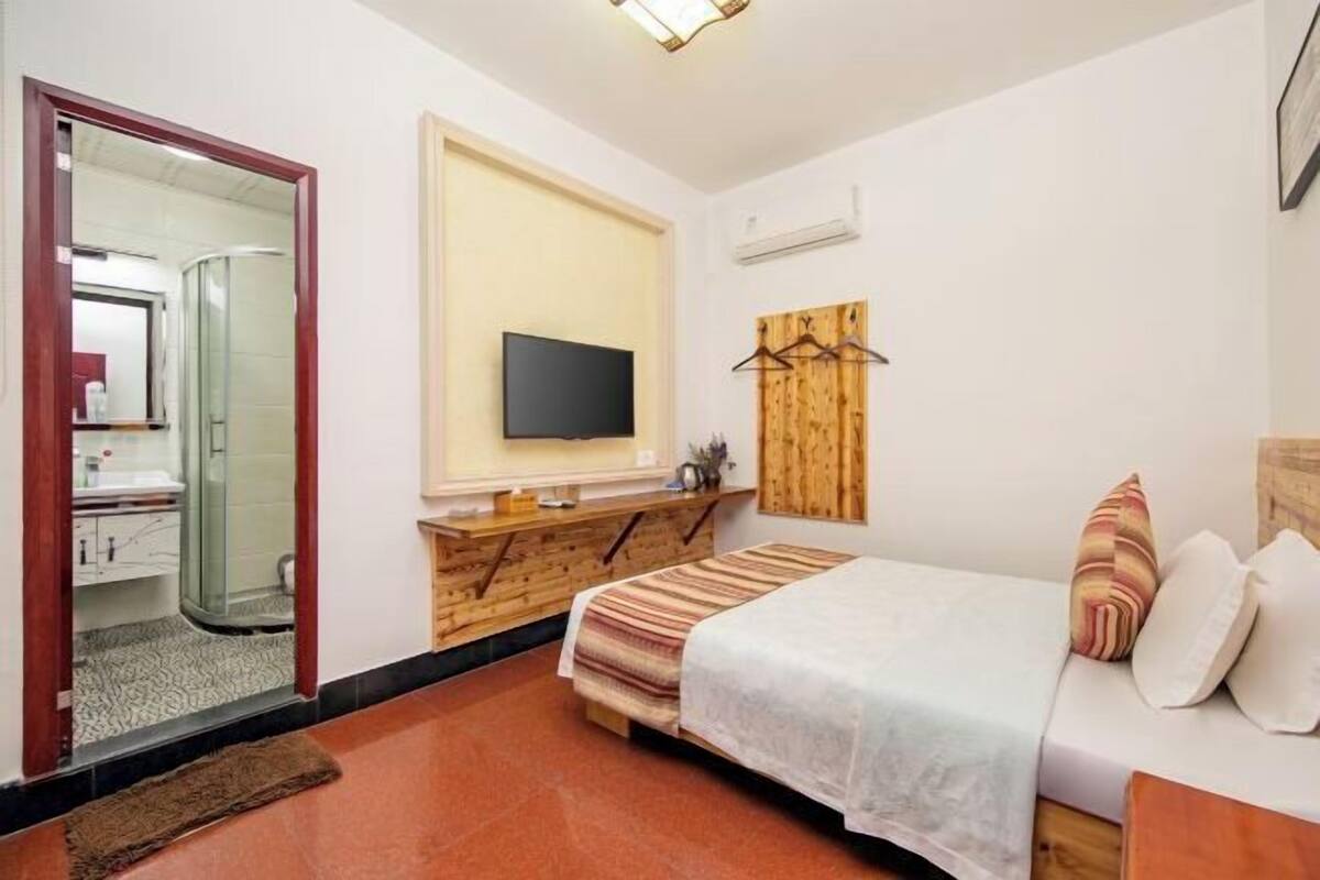 A bedroom with a bed, a TV mounted on the wall, a wooden dresser, a mirror, and a wooden panel on the wall.