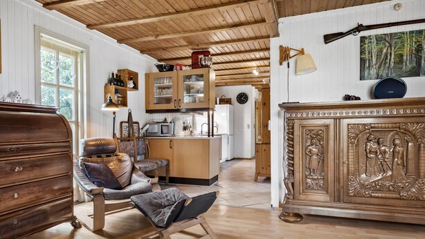 A spacious room with wooden floors, a large wooden cabinet with intricate carvings, a comfortable leather sofa, and a dining area with a wooden table and chairs. - Amazing home in Sydals with WiFi (Sydals)