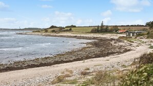 A coastal landscape with a sandy beach, rocky shore, and a few buildings in the background. - Amazing home in Sydals with WiFi (Sydals)