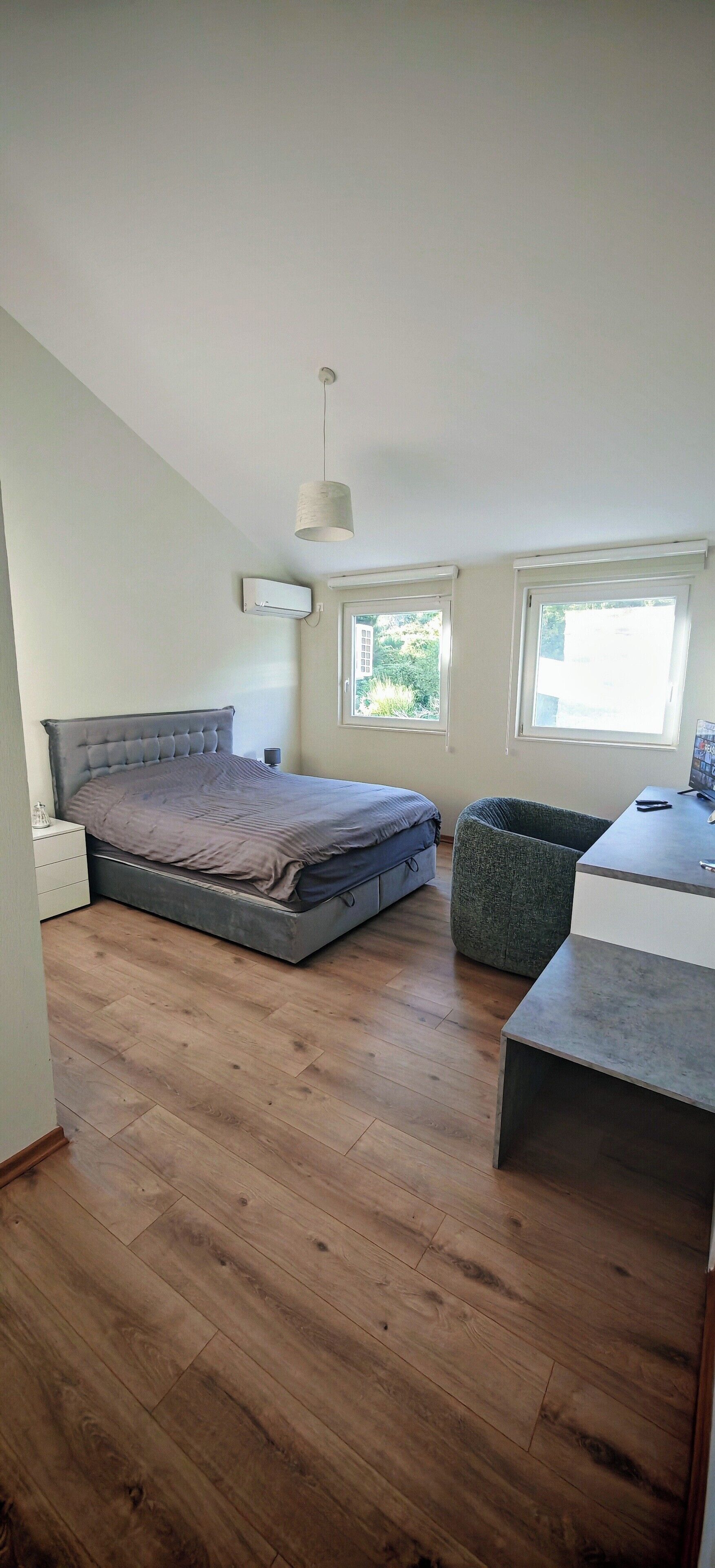 Une chambre à coucher comprenant un lit, une table de chevet, une chaise, un bureau et deux fenêtres.