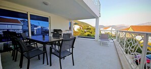 Een balkon met een tafel en stoelen, een barbecue en uitzicht op het omliggende landschap.