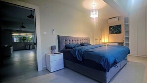 Een moderne slaapkamer met een groot bed, nachtkastjes, een plafondlamp, een aan de muur bevestigde televisie en een raam met uitzicht op groen.