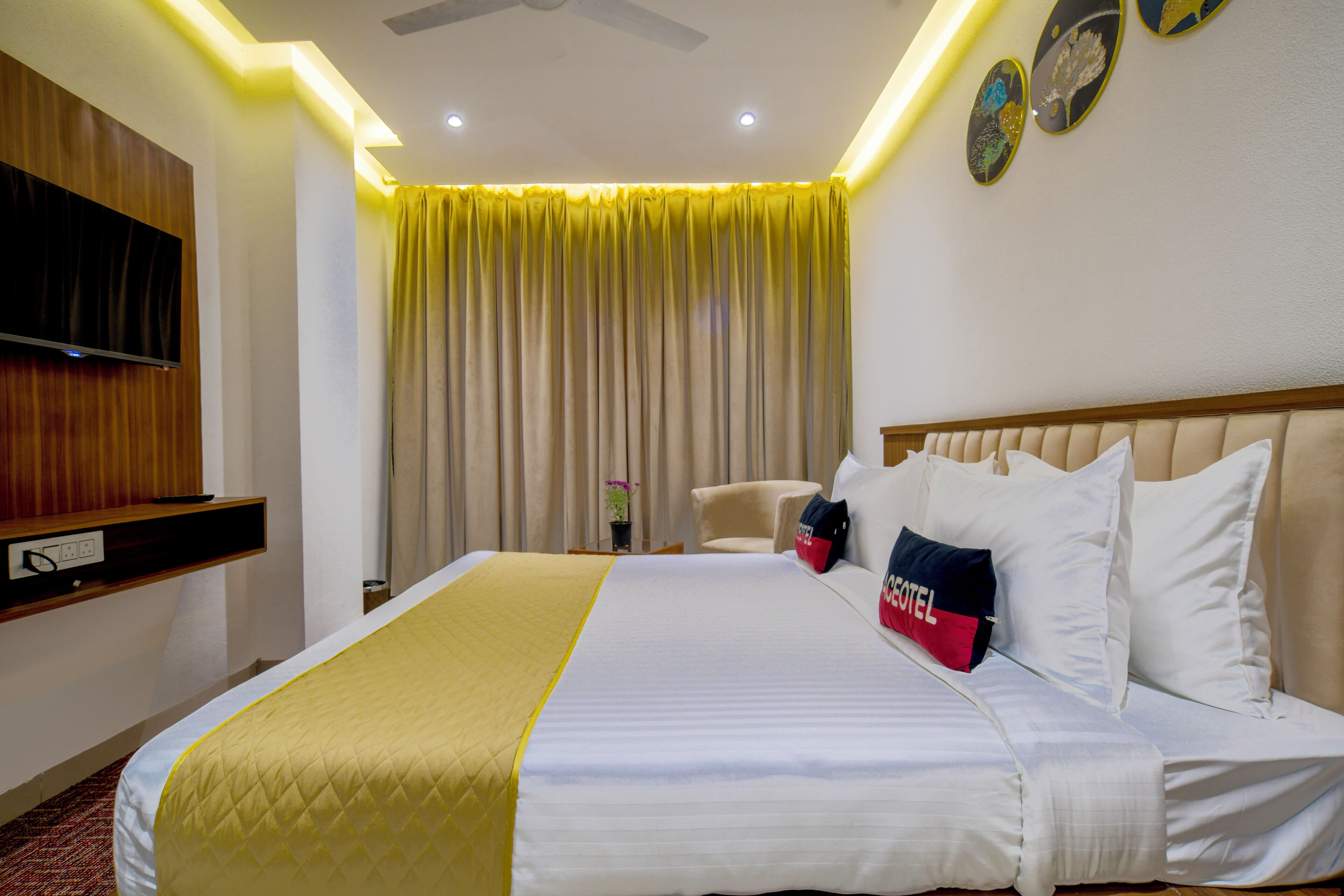 Habitación de hotel con cama, televisión montada en la pared, ventilador de techo y ventana con cortinas.