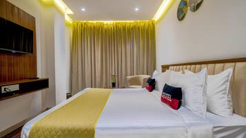 Habitación de hotel con cama, televisión montada en la pared, ventilador de techo y ventana con cortinas.