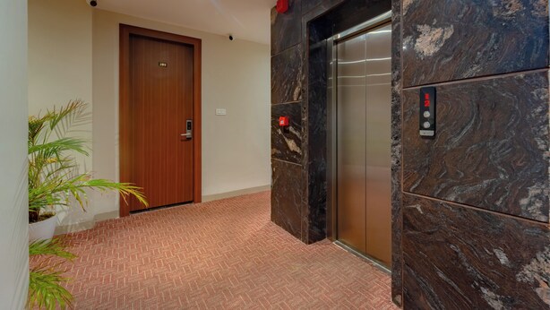 A hallway with a wooden door labeled "20", a marble elevator, and a potted plant. - Aceotel Premier Vijay Nagar (Indore)