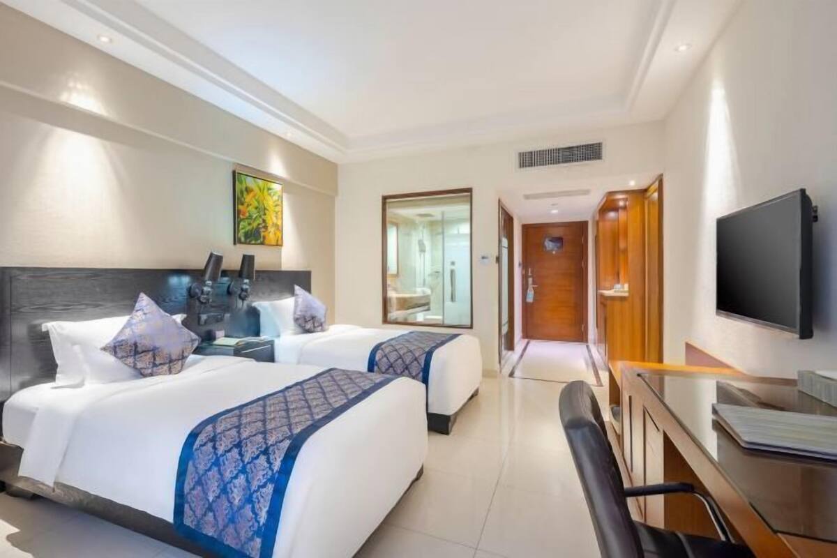 Une chambre d’hôtel avec deux lits, un bureau, une chaise, une télévision et une salle de bain visible à travers une porte ouverte.