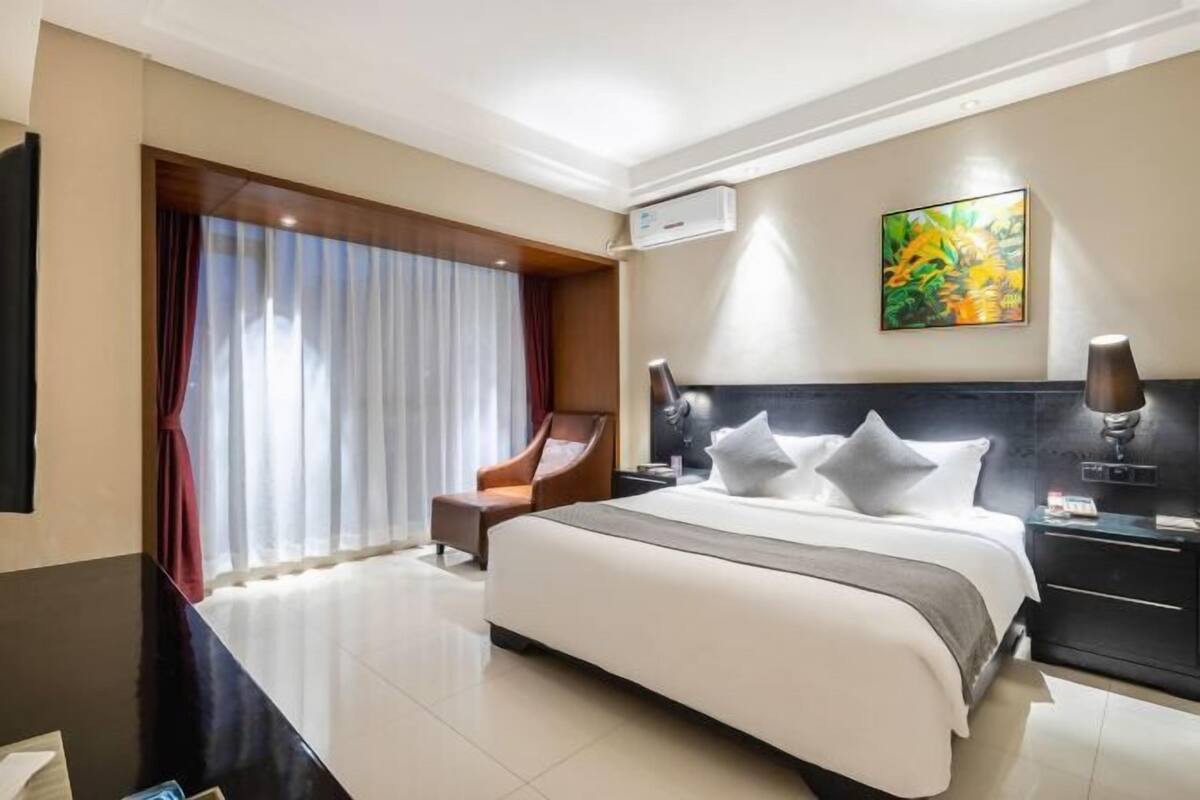 Une chambre d’hôtel moderne avec un grand lit, un bureau, une chaise et un tableau au mur.