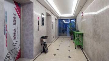 A hotel corridor with a trash bin, a green cart, and a glass door leading to a room.