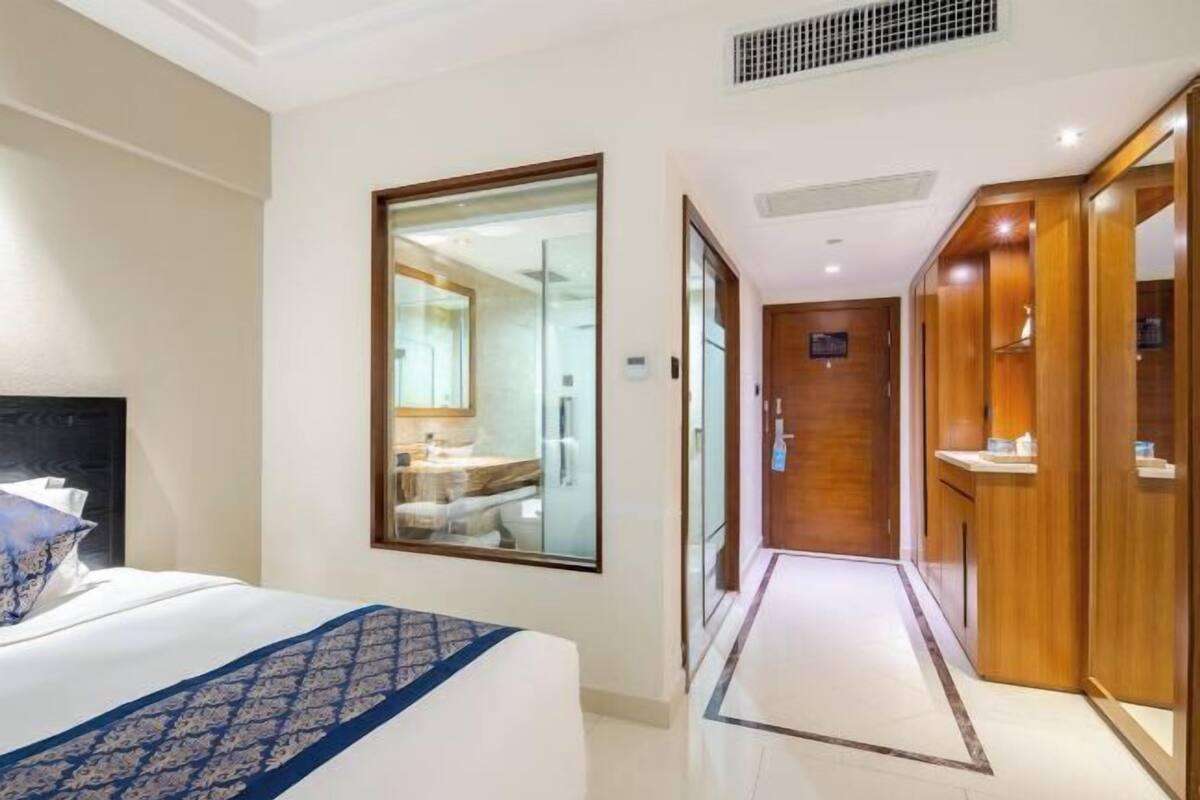 Une chambre d’hôtel avec un lit, un grand miroir, une salle de bain visible à travers le miroir et une armoire en bois.