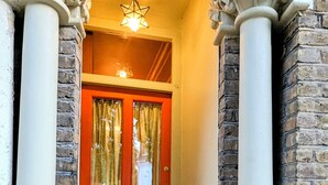 A red door with a star-shaped light fixture above it, flanked by white columns with decorative capitals, leading to a brick wall entrance. - Charming East London Apartment (London)