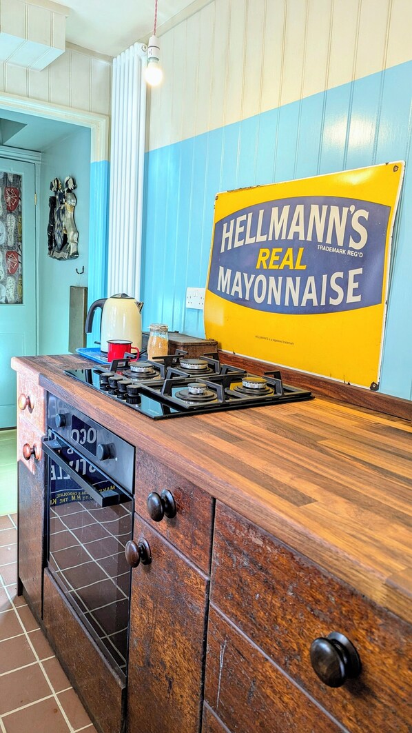 Keittiössä on vanhanaikainen liesi, vedenkeitin ja kyltti, jossa mainostetaan Hellmann’sin aitoa majoneesia.