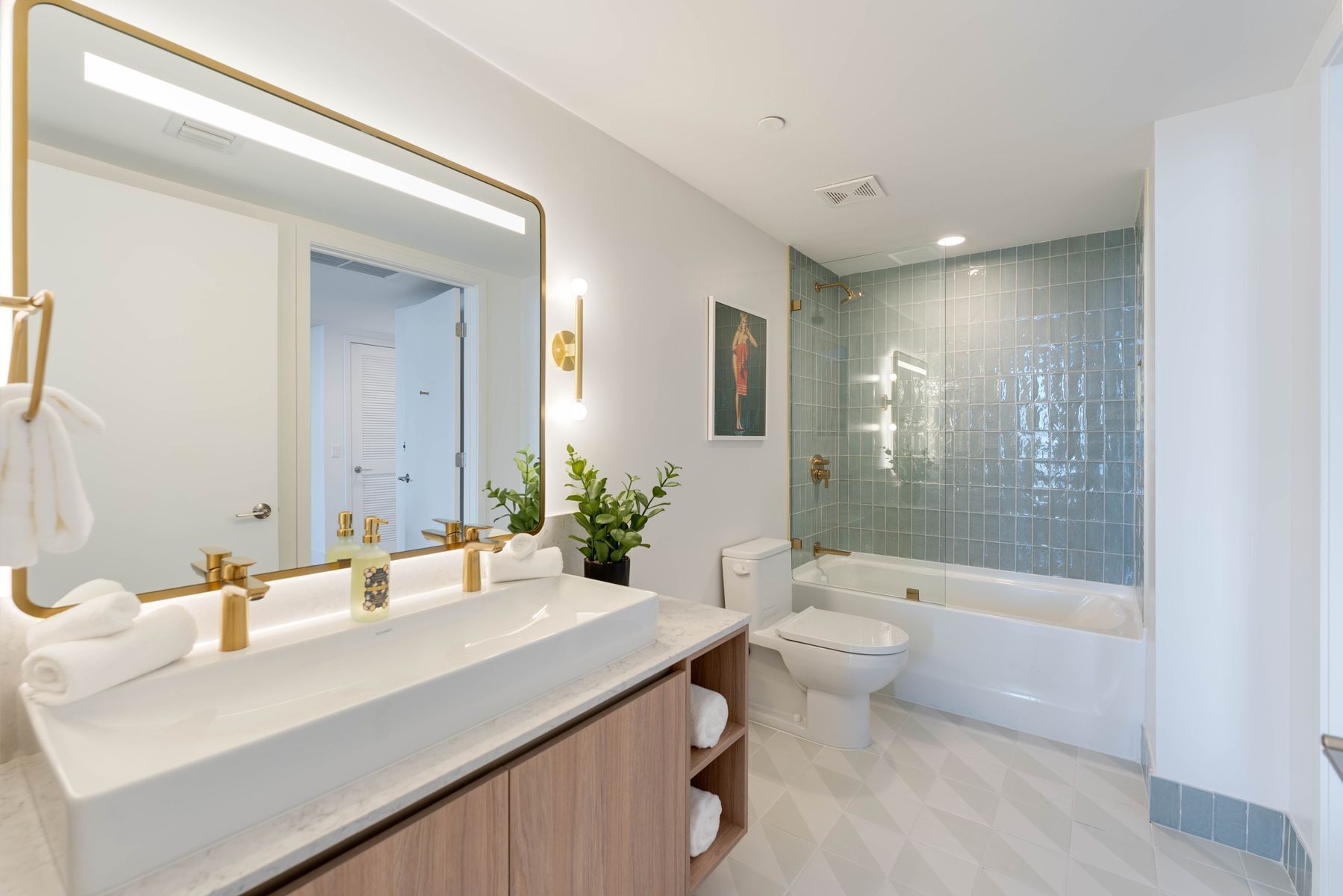 A modern bathroom with a large mirror, dual sinks, a toilet, and a bathtub.