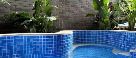 A swimming pool with blue tiles, surrounded by plants and a brick wall.