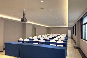 A conference room with rows of tables and chairs, a projector, and a door in the background. - Huquan Bund Hotel (Mile)