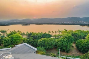 Vista de un lago al atardecer, rodeado de vegetación y edificios a lo lejos.