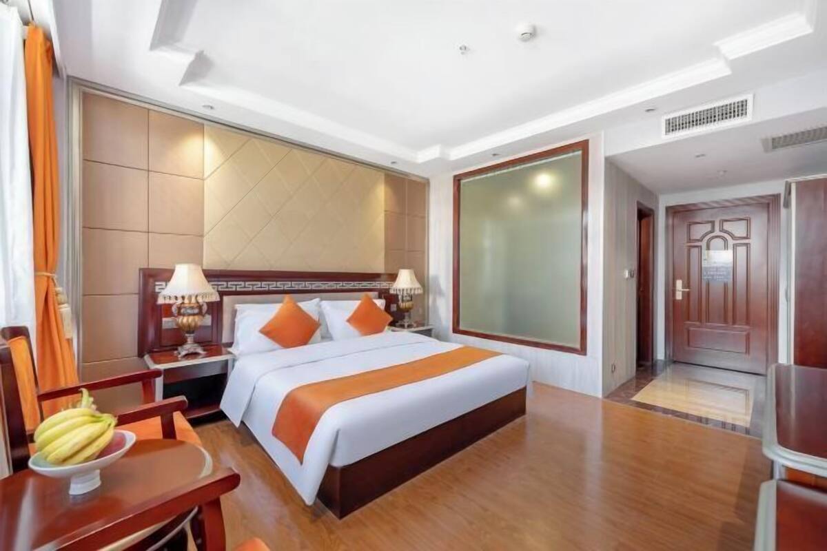 A hotel room with a large bed, wooden headboard, two bedside tables with lamps, a wooden desk, and a chair.