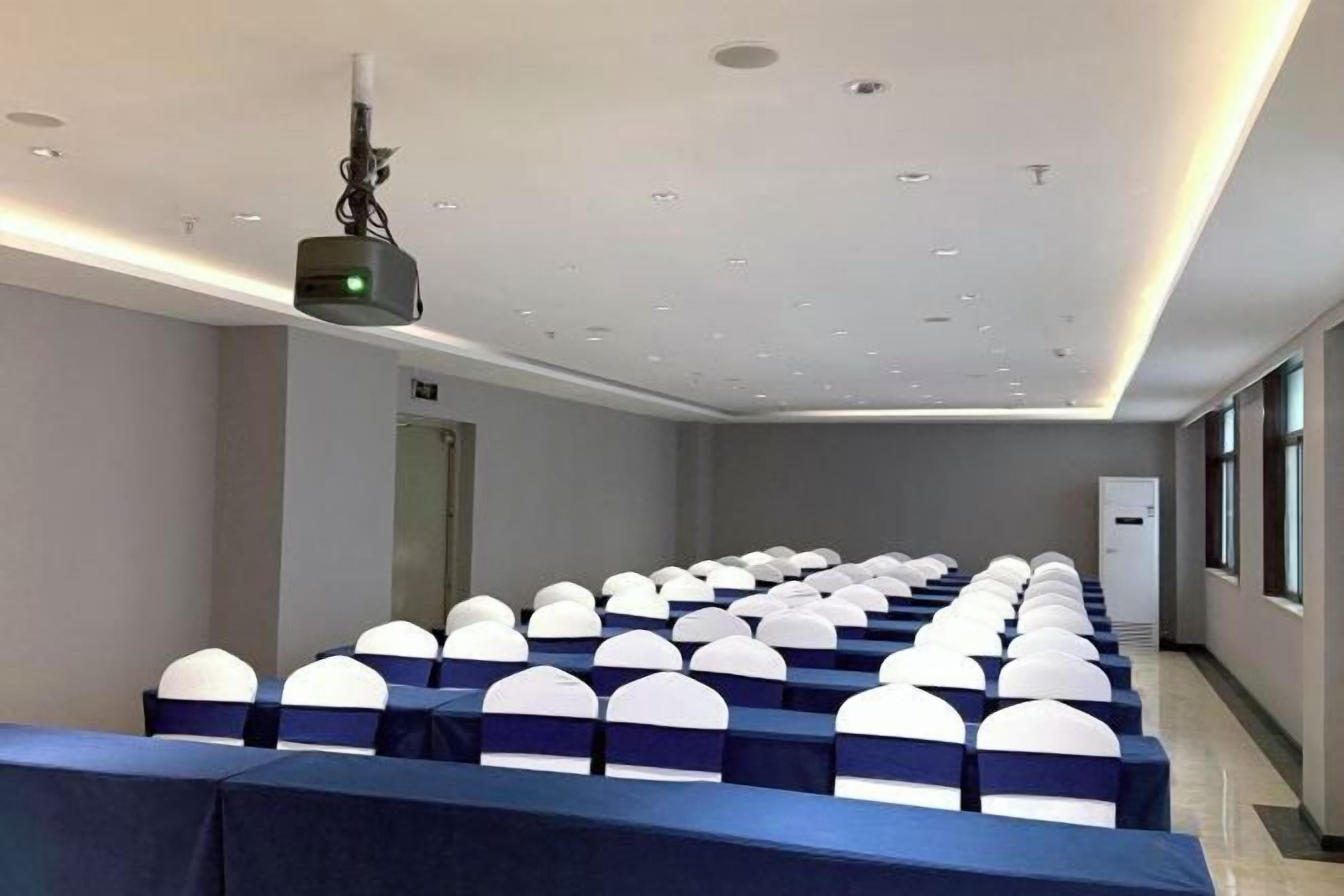 A conference room with rows of tables and chairs, a projector, and a door.