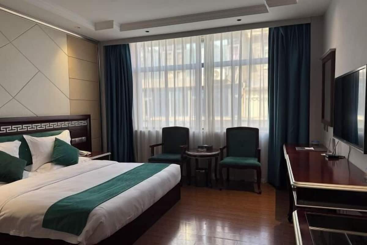 A hotel room with a bed, two chairs, a small table, a TV, and a window with curtains.