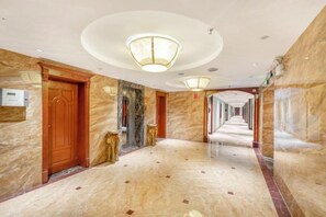 A hotel corridor with marble flooring, wooden doors, and a central light fixture. - Huquan Bund Hotel (Mile)