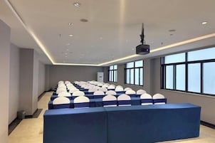 A conference room with rows of blue chairs, a large screen, and windows along one wall.