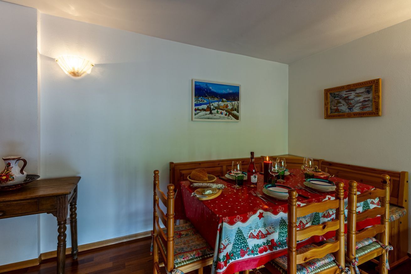 Een eethoek met een tafel voor vier personen, houten stoelen, een bijzettafeltje van hout en een wandlamp.