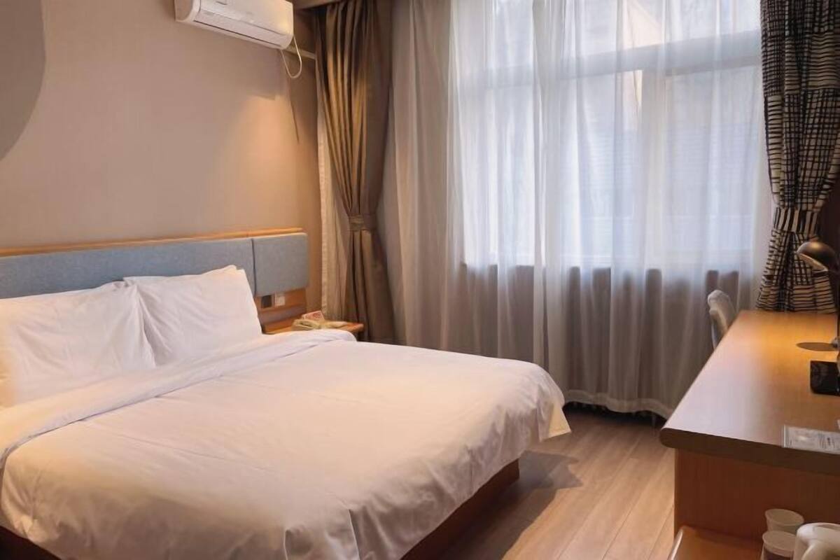 Une chambre d’hôtel avec un lit, un bureau, une chaise et une fenêtre avec des rideaux.