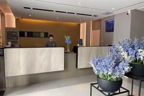 Zona de recepción con mostrador, una persona atendiendo y plantas en macetas.