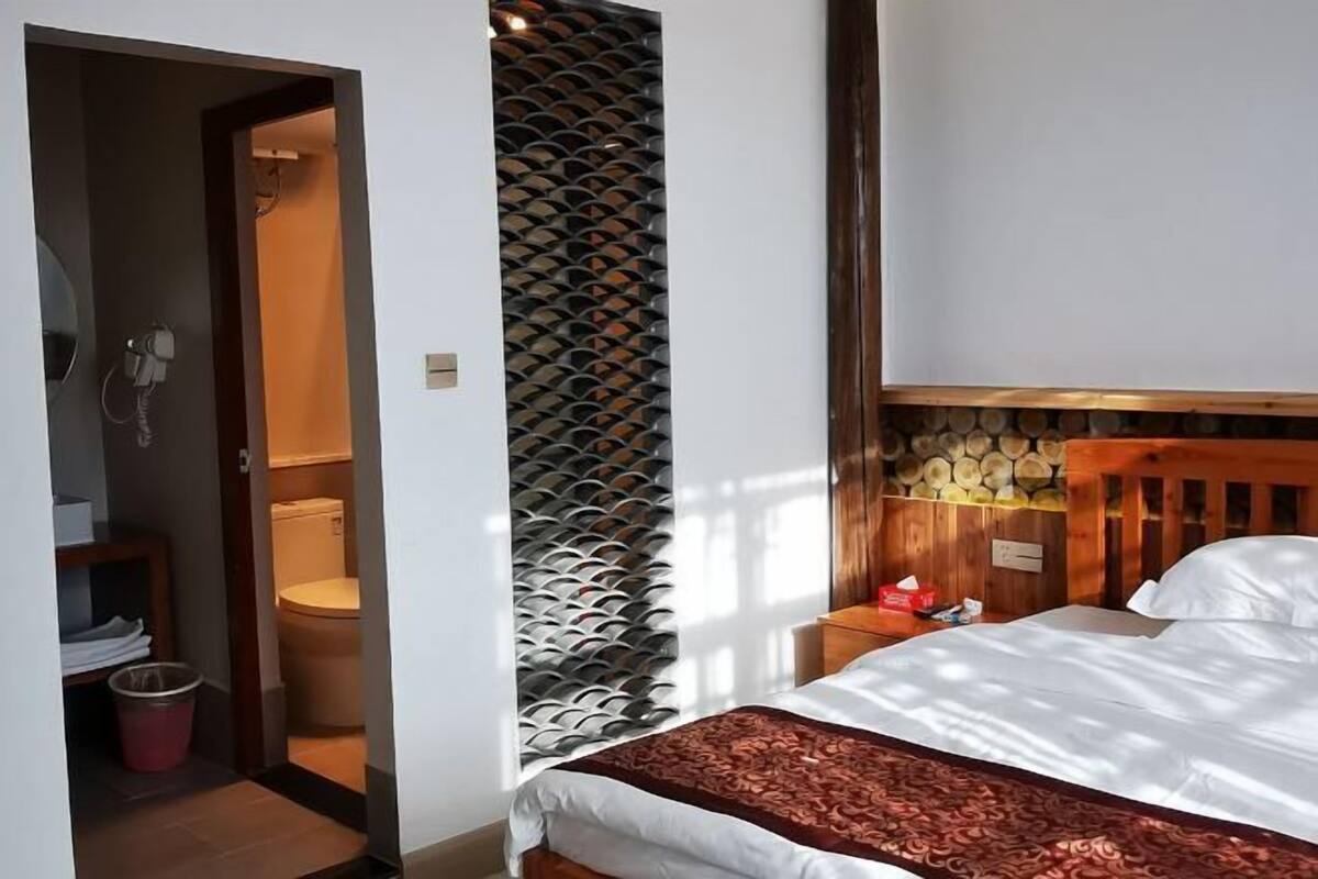 Habitación de hotel con cama, cabecero de madera, mesita de noche pequeña y un calentador fijado a la pared.
