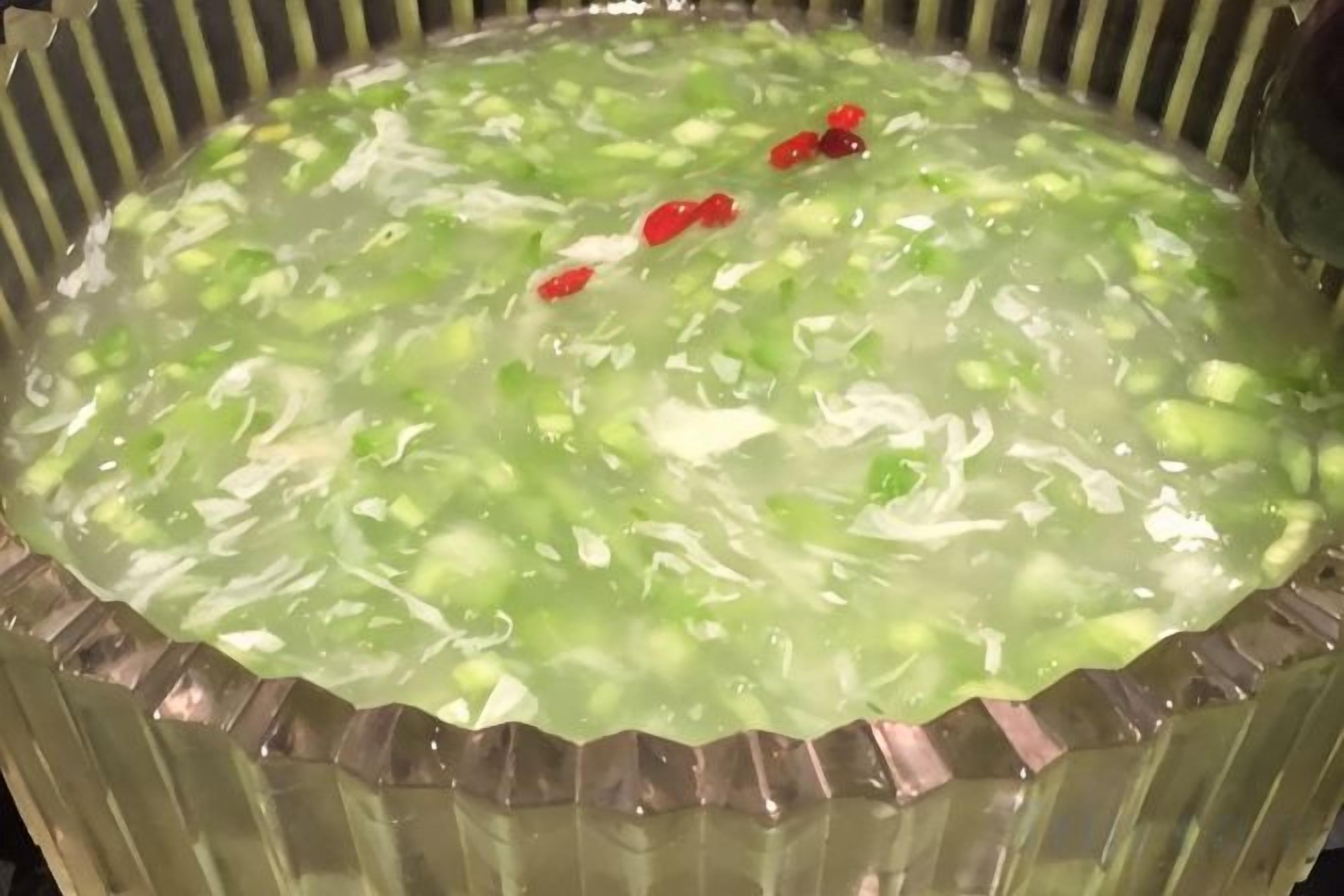 A bowl of clear liquid with green and red elements, possibly a beverage or soup.