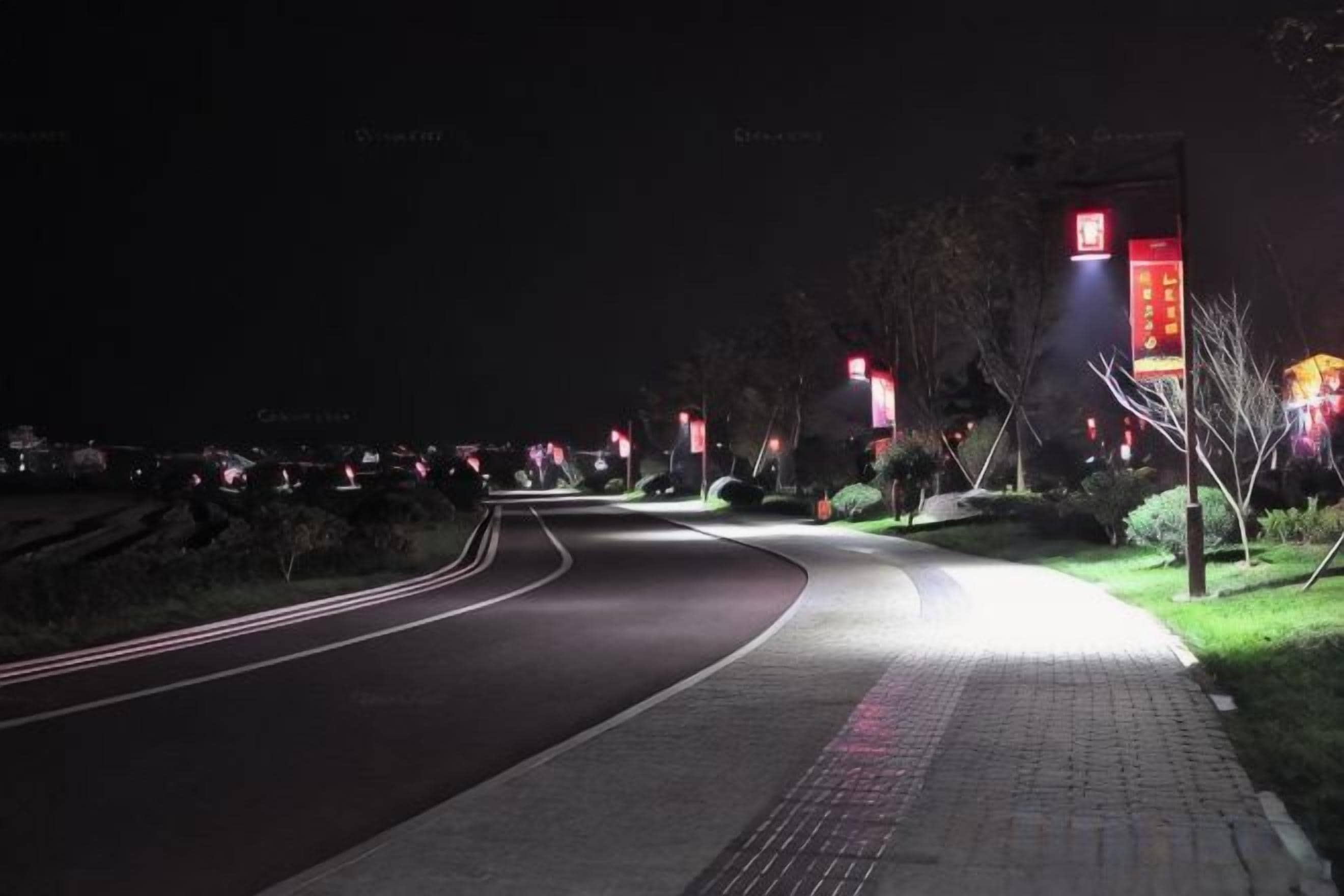 Uma estrada à noite com calçada e placas iluminadas.