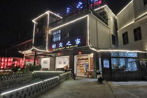 Un edificio con señalización iluminada, entrada protegida por un portón y escaparates visibles.