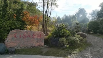 A paved pathway leading through a landscaped area with a stone marker and various shrubs and trees.