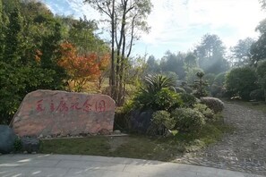 Un sendero pavimentado que atraviesa un área ajardinada con un hito de piedra y diversos arbustos y árboles.