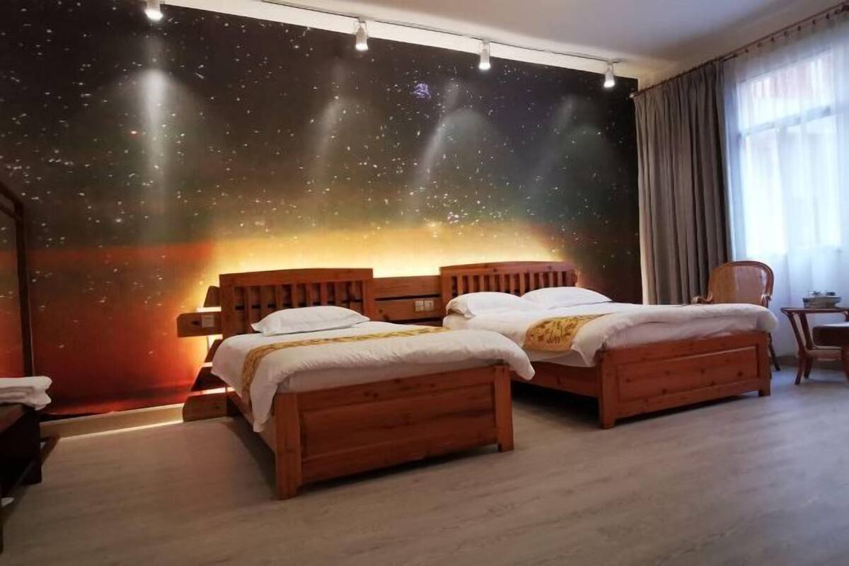 Una habitación con dos camas de madera, un mural de cielo nocturno en la pared y una ventana con cortinas.