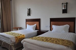 Habitación de hotel con dos camas individuales, una mesita redonda y un reloj en la pared.