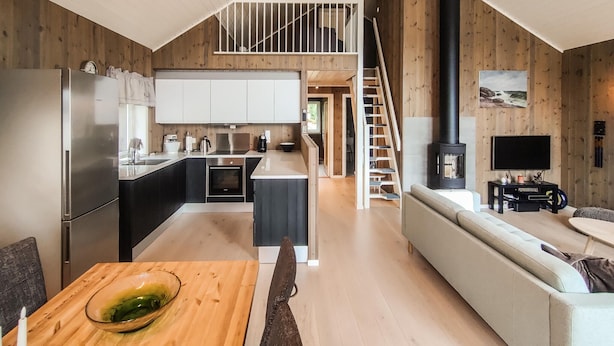 Une cuisine moderne avec un îlot central, un coin repas avec une table en bois, un canapé et un espace détente avec un téléviseur et une cheminée.