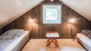 Une petite chambre mansardée avec des murs en bois, un plafond en pente, une seule fenêtre et deux lits.
