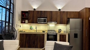 Une cuisine moderne avec des meubles en bois, un four à micro-ondes encastré, une cuisinière et un réfrigérateur. Il y a également un coin salon avec un ventilateur et une fenêtre donnant sur un paysage agréable.