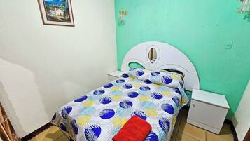 A bedroom with a bed, a nightstand, a wall-mounted light, and a framed picture.