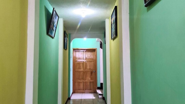 Un pasillo con paredes verdes, una puerta de madera al final y cuadros en las paredes.