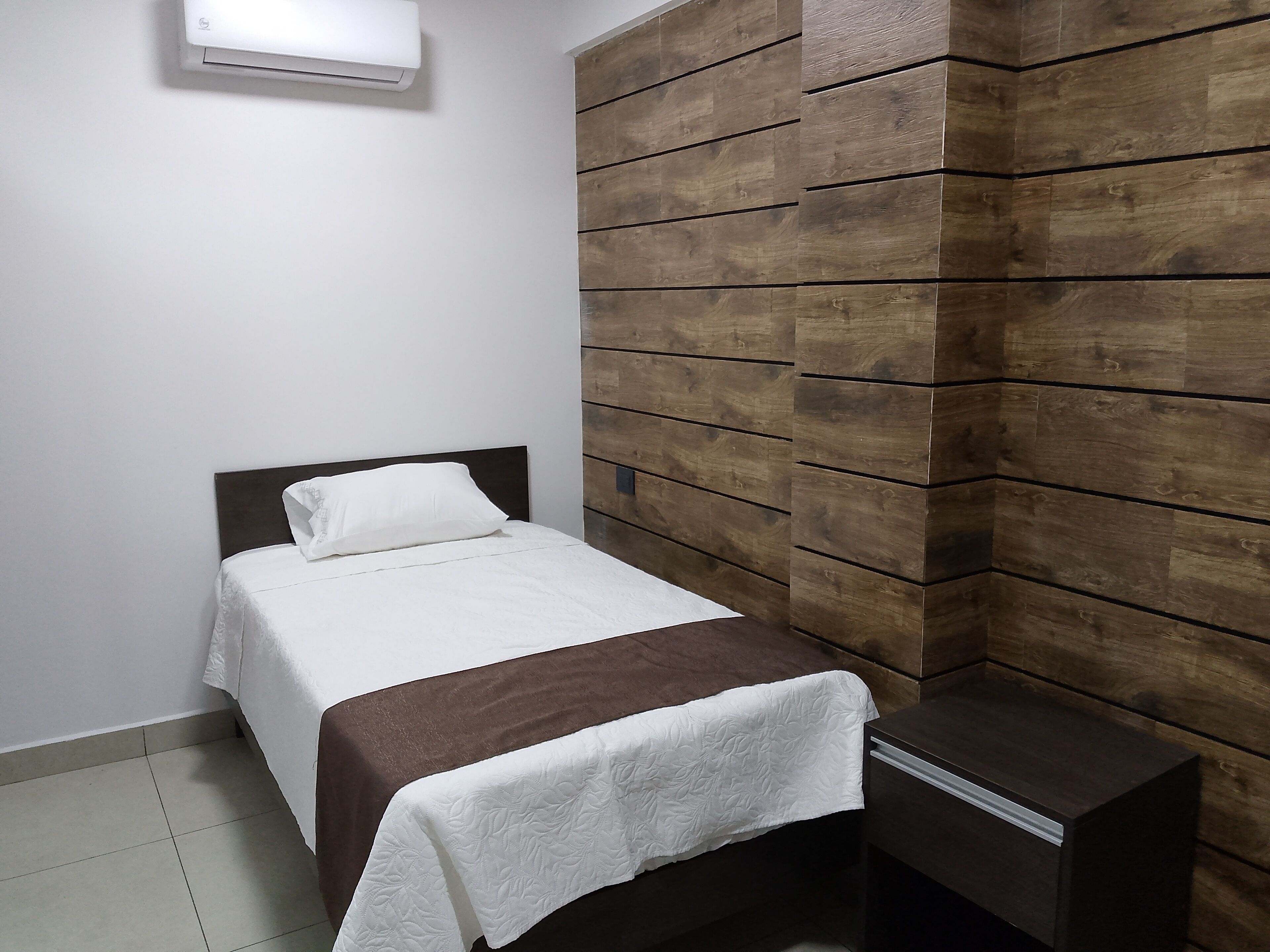 Ein Schlafzimmer mit einem Bett, einem Nachttisch, einer Holzwand und einer Klimaanlage.