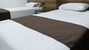 A hotel room with two beds, each with a pillow and a blanket. The room has a wooden headboard and a white wall.